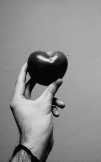 Cropped image of hand holding tomato against wall