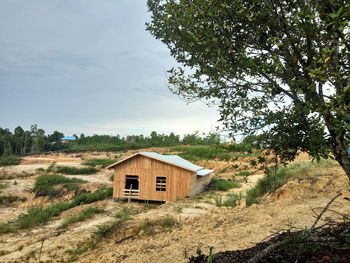 House on field by trees against sky