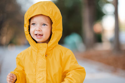 Cute funny kid girl 2-3 year old wear yellow rain jacket with hood in autumn park outdoor.