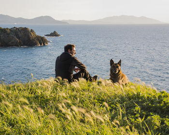 Rear view of man with dog on beach against sky