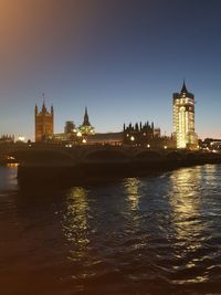 Illuminated buildings by river against sky in city