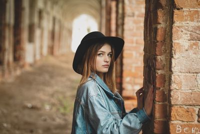 Portrait of beautiful young woman standing against brick wall