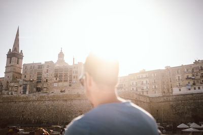 Rear view of mature man looking at building in city against sky