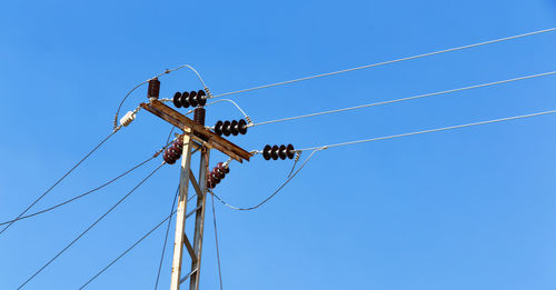 Low angle view of electricity pylon against clear blue sky