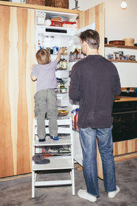 Boy searching in refrigerator while standing with father in kitchen at home