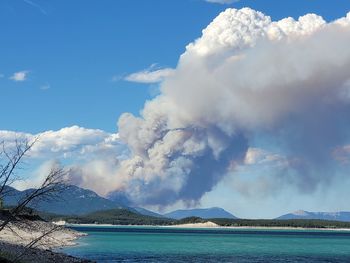 Scenic view of lake against sky with large plume of wildfire smoke 