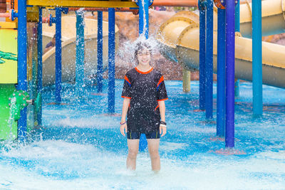 Teenage girl standing below falling water at park