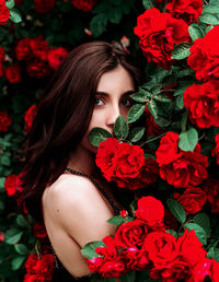 Portrait of a beautiful girl among the bush of the red rose