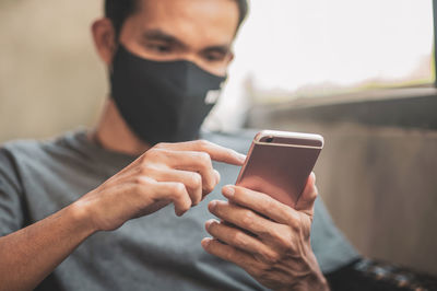 Man wearing mask using smart phone sitting at home