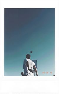 Rear view of man sitting against blue sky