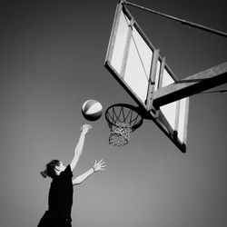 Low angle view of woman playing basketball against clear sky