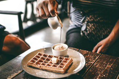 Midsection of man pouring sauce in waffle on table in restaurant