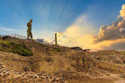 Statue on rock on land against sky