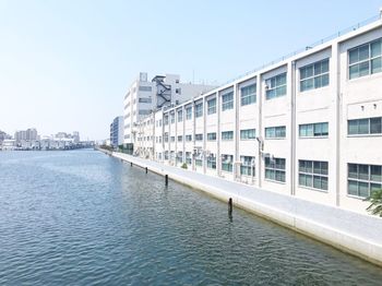 Modern buildings by river against clear sky