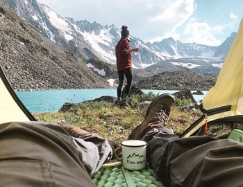 Low section of man sitting on mountain against sky