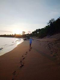 Rear view of man on beach against sky during sunset