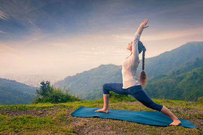 Full length of woman sitting on mountain against sky during sunset