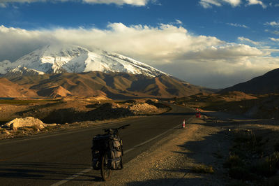 People riding on road by snowcapped mountain against sky