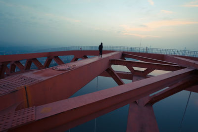 Man walking on bridge over river against sky