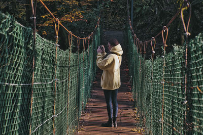 Rear view of man standing on footbridge in forest