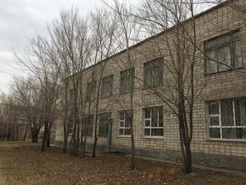 Bare trees by old building against sky