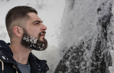 Side view of young man standing against waterfall