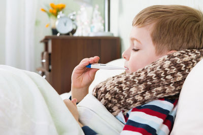 Cute boy holding thermometer in mouth at home