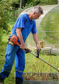 Worker with a hand trimmer in his hands mows the grass in front of the house. lifestyle.