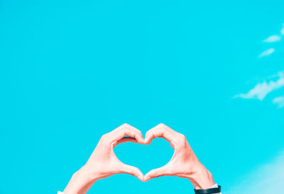 Close-up of hand holding heart shape against blue background