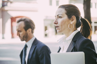 Businesswoman looking away while walking with coworker in city