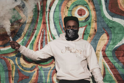 Portrait of young man standing against graffiti wall