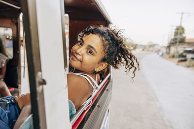 Smiling carefree girl leaning out of window while traveling in tuk-tuk on vacation