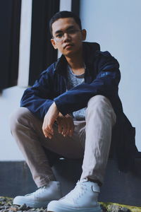 Low angle portrait of young man sitting on seat against wall