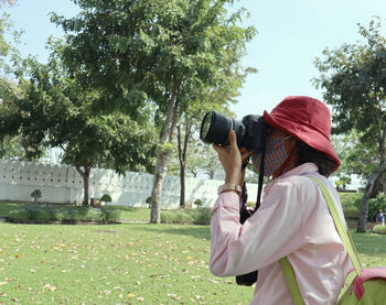 Side view of woman photographing against trees
