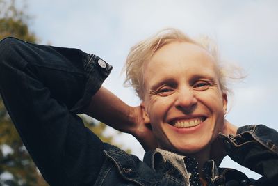 Portrait of smiling mid adult woman with hands behind head against sky