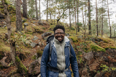 Happy mature man with backpack standing in forest during vacation