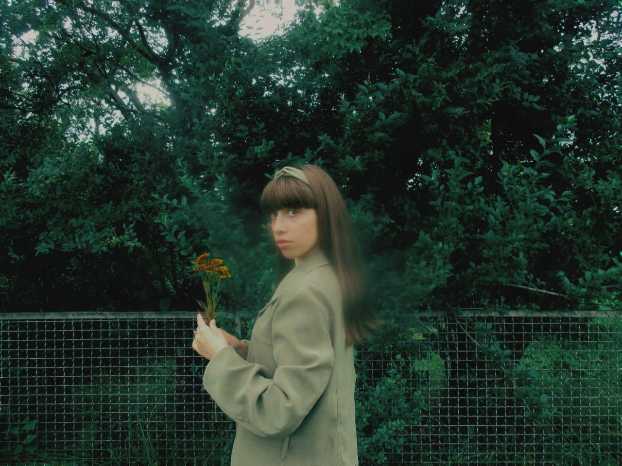 green, plant, one person, tree, young adult, standing, nature, forest, women, sunlight, spring, growth, waist up, adult, leisure activity, fence, looking, lifestyles, leaf, clothing, person, three quarter length, outdoors, side view, casual clothing, day, hairstyle, flower, female, holding, darkness, grass, snapshot, light