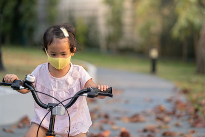 Little girl wearing anti pollution mask on her bike at park.