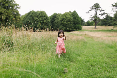 Portrait of girl walking on grass at meadow against sky