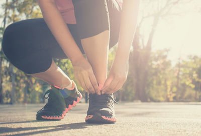 Low section of woman tying shoelace on road