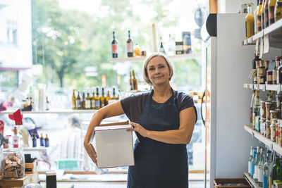Portrait of confident female owner carrying cardboard box in deli