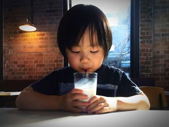 Close-up of boy drinking milk at dining table against wall