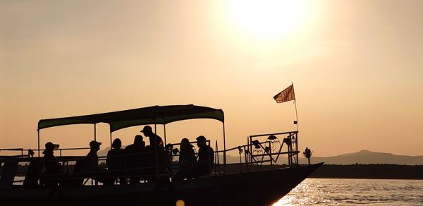 Silhouette people on boat against sky during sunset