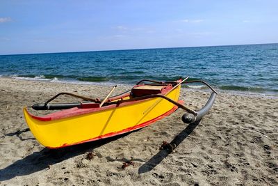 Outrigger boat moored on shore at beach against sky