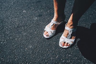 Low section of woman standing on road during sunny day