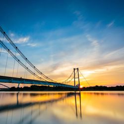 Silhouette bridge over calm sea at sunset