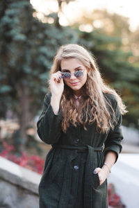 Smiling young woman wearing sunglasses standing with hand in pocket