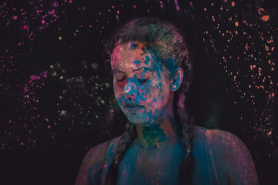 Close-up of woman with powder paint on face against black background