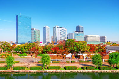 Trees and modern buildings in city against blue sky