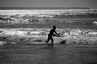 Silhouette man walking with surfboard at sea